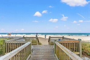A wooden boardwalk leading to a beach with a clear sky.