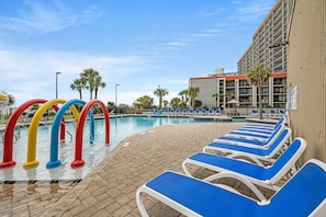 A swimming pool with colorful water slides, lounge chairs, and a building with balconies.