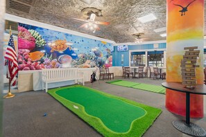 A room with a green artificial turf, a white bench, a table with a stack of bricks, and a mural with marine life.