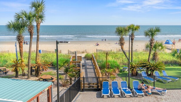 Uitzicht op een strand met palmbomen, een houten terras en lounge stoelen.