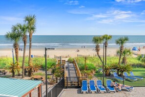 Une vue sur la plage, avec des palmiers, une terrasse en bois et des chaises longues.