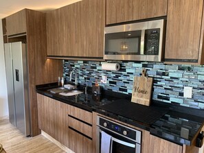 Een moderne keuken met houten kastjes, een roestvrijstalen koelkast, een magnetron, een broodrooster en een betegelde achterwand.