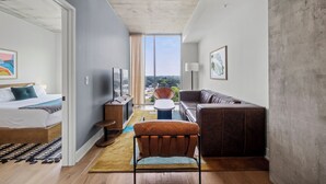 Et moderne hotelværelse med seng, sofa, stol og skrivebord. Der er et stort vindue med udsigt over byen.