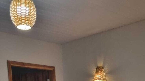 A neatly made bed with white linens and towels, a wooden door, a wall-mounted light fixture, and a red and black flower-patterned rug. - Pousada Estância da Mata (Nobres)
