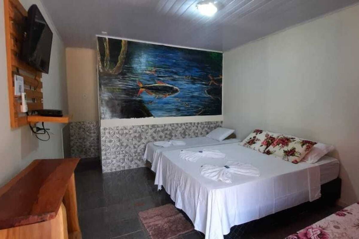 Habitación con dos camas, un televisor montado en la pared y un mural que representa un paisaje fluvial.