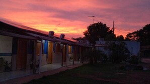 A row of single-story buildings with a flat roof, likely a motel or small hotel, with a clear sky in the background. - Pousada Estância da Mata (Nobres)