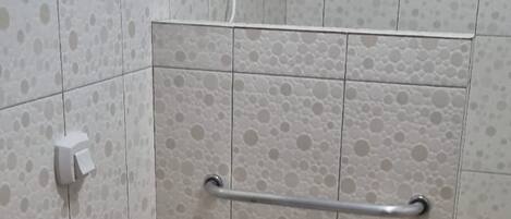 A bathroom with a toilet, a handrail, a sink, and a shower.