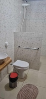Casa de banho com sanita, barra de apoio, lavatório e chuveiro.