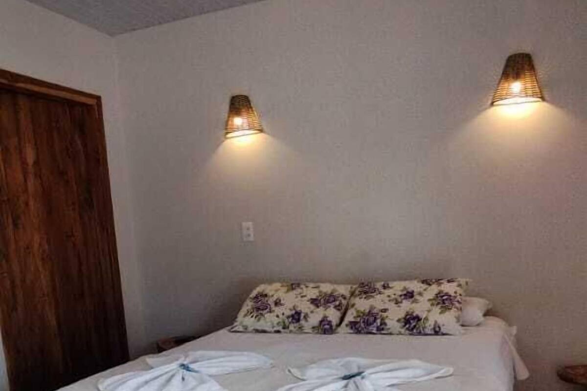 Un dormitorio con una cama, dos lámparas fijadas a la pared, una puerta de madera y un tapete rojo con forma de corazón.