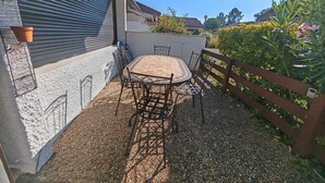 Une terrasse extérieure avec une table et des chaises, entourée d’une zone recouverte de gravier et d’une clôture en bois.