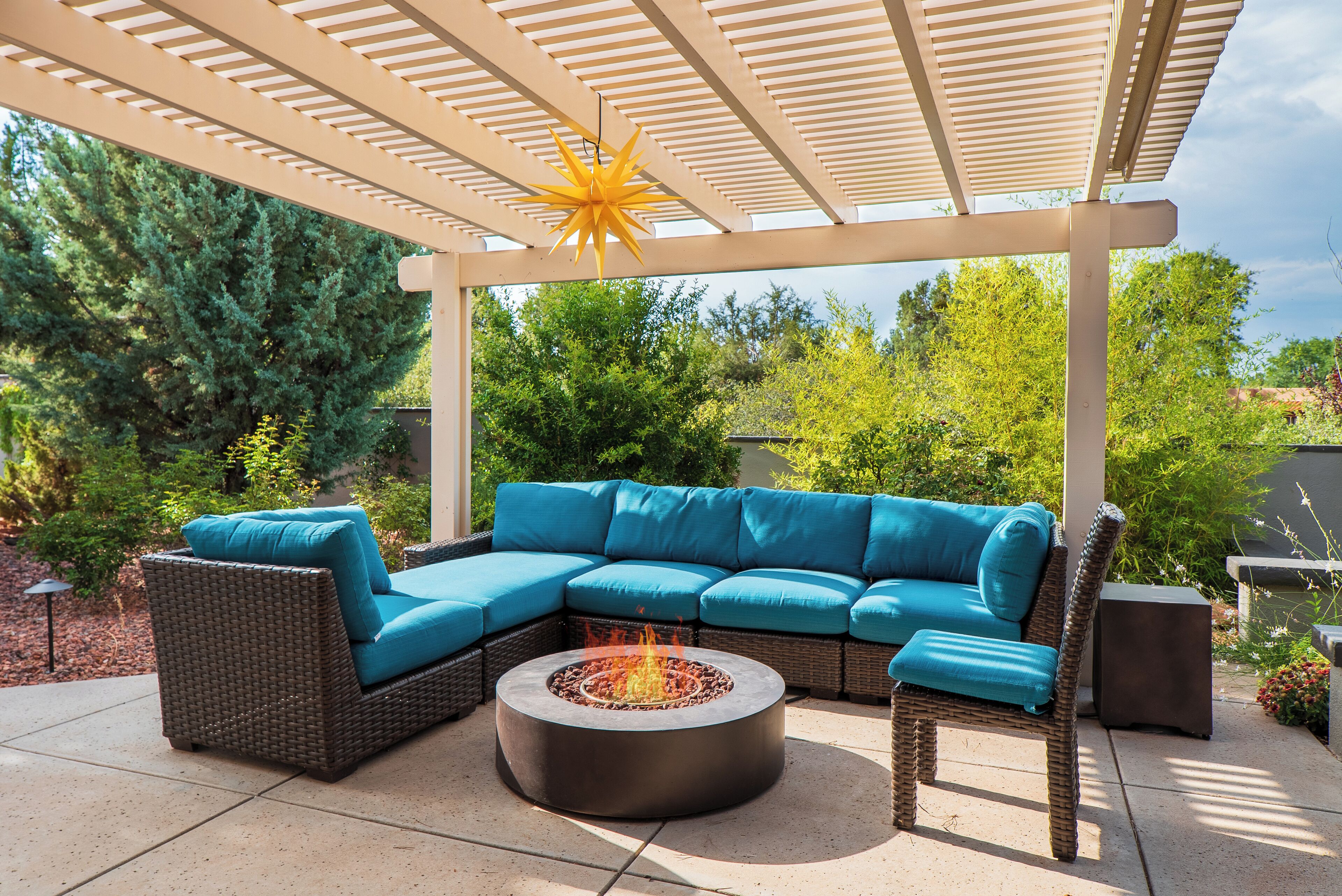 Un patio exterior con un sofá modular, un pozo de fuego redondo y una pérgola con una lámpara en forma de estrella.