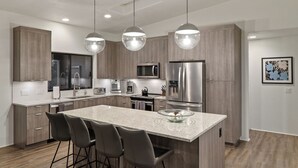 A modern kitchen with a large island, bar stools, stainless steel appliances, and pendant lighting.