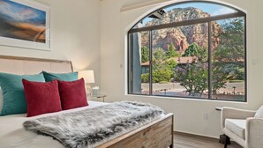 A bedroom with a large window, a bed with a fur throw, and a view of a mountainous landscape.