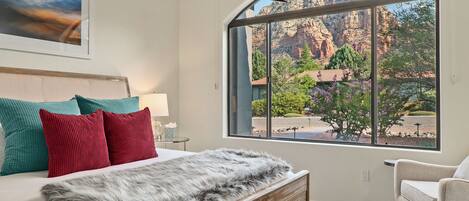 A bedroom with a large window, a bed with a fur throw, and a view of a mountainous landscape.
