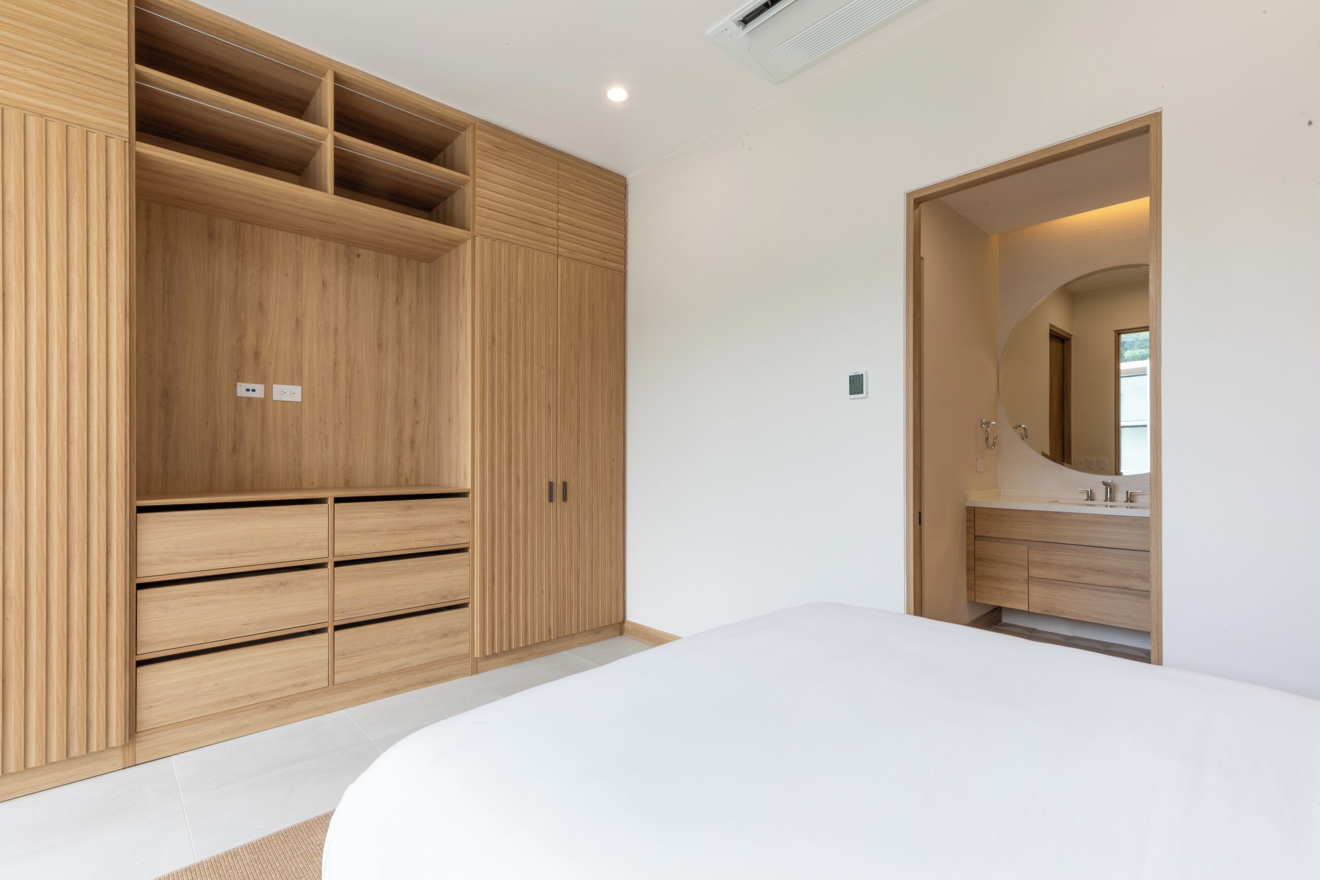 A bedroom with a large wardrobe, a bed, and a bathroom with a mirror and sink.