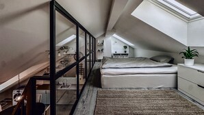 Une chambre de style loft, à la fois compacte et moderne, dotée d’une lucarne, d’un lit, d’un petit bureau et d’une plante en pot.