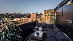 Une terrasse sur le toit avec un canapé de couleur sombre, une table basse en osier et une plante en pot.