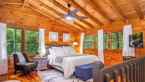 A wooden cabin bedroom with a bed, a chair, a desk, and a TV. - Cabin Getaway: Hot Tub, Hiking, Pet-Friendly, Pool Table/Games, & Yoga Room (Blue Ridge)