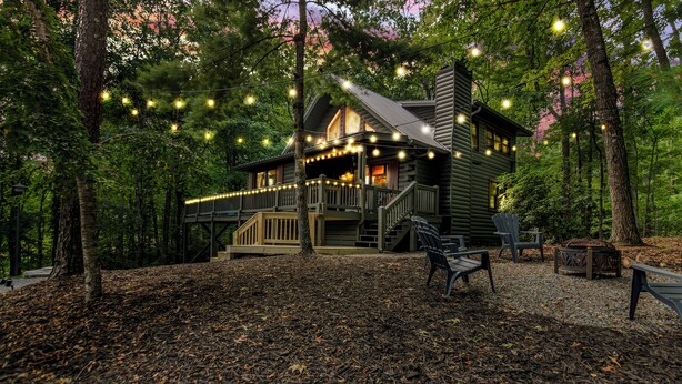 Eine Holzhütte mit Veranda und Lichterketten, umgeben von Bäumen und einem mit Laub bedeckten Boden.