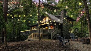 Eine Holzhütte mit einer Terrasse, umgeben von Bäumen und Lichterketten.