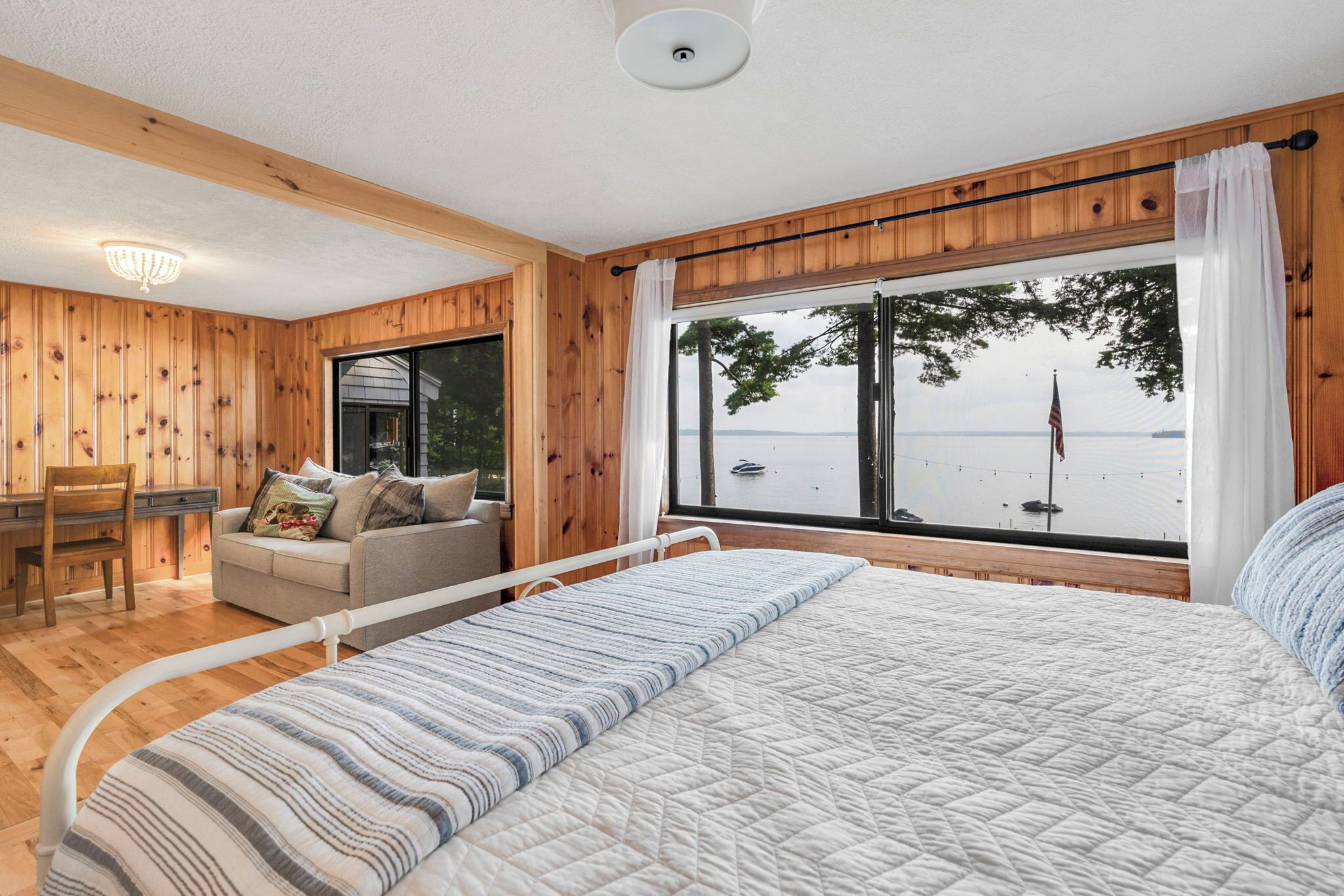 A bedroom with a large bed, a wooden desk, a chair, and a view of the water.