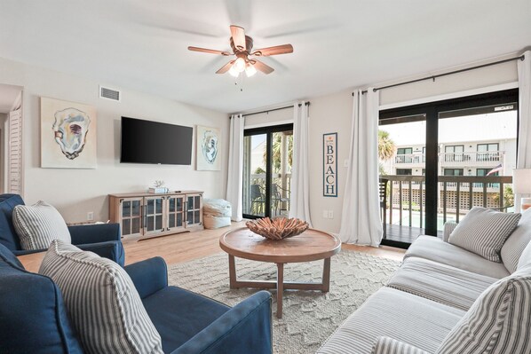A living room with a ceiling fan, a flat-screen TV, a round coffee table, and a sofa.