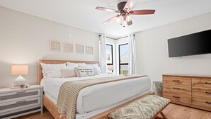 Ein Schlafzimmer mit Bett, Nachttisch, Bank, Kleiderschrank, Deckenventilator und Fernseher an der Wand.