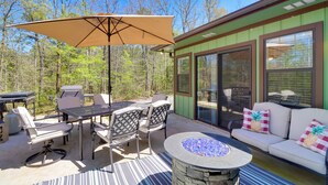 An outdoor patio with a table and chairs, a fire pit, and a covered area with an umbrella. - Lakeside Retreat on 10 Secluded Wooded Acres, Hot Tub, Level 2 EV Charger (Greers Ferry)