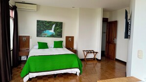 A hotel room with a bed, a wooden floor, a painting of a waterfall, a wooden wardrobe, and a small table. - Legacy Boutique Hotel (Quesada)