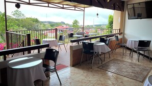 A covered outdoor seating area with tables and chairs, a view of greenery and buildings in the distance, and a tiled floor. - Legacy Boutique Hotel (Quesada)