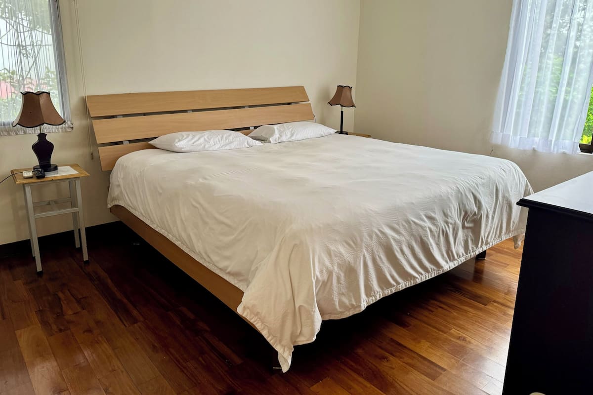 Un lit bien fait, avec du linge de lit blanc, dans une pièce dont le sol est recouvert de parquet.