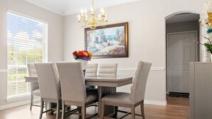 Un coin repas avec une table ronde, six chaises, un lustre et un tableau au mur.