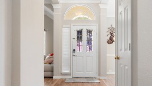 Un couloir avec une porte blanche, une petite fenêtre surmontée d’une vitre et un élément décoratif mural.