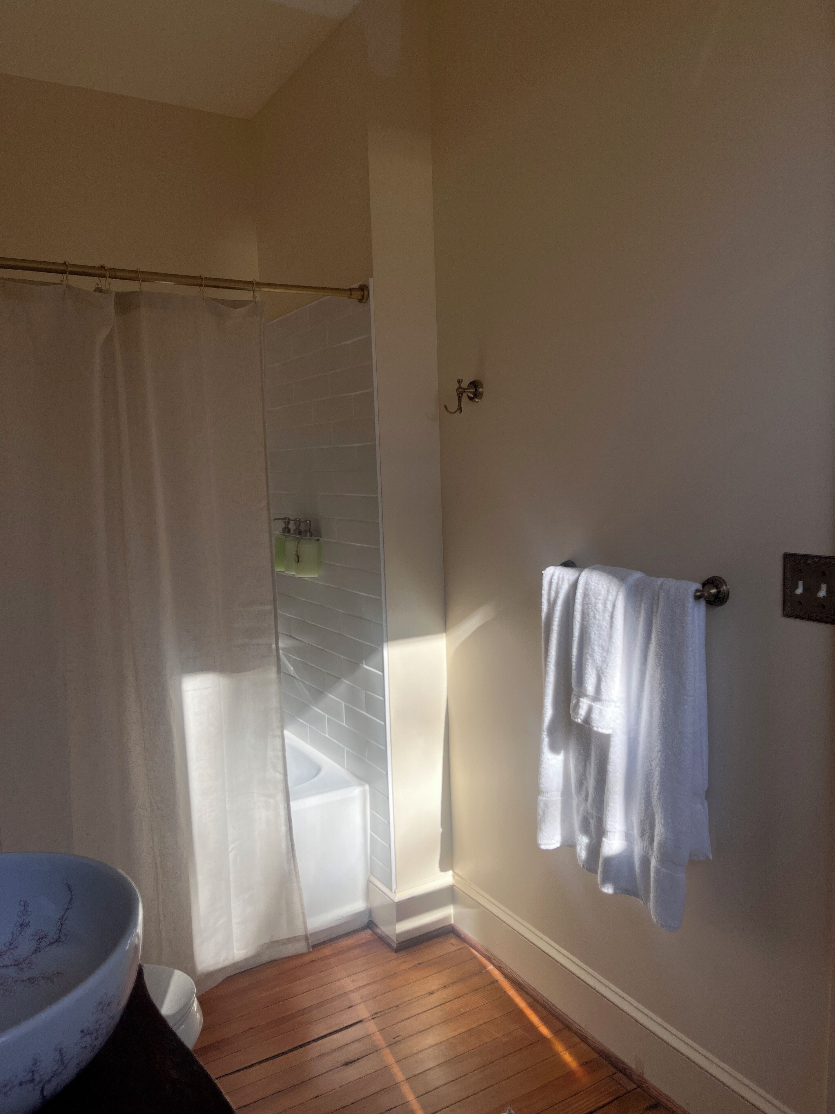 Een badkamer met een houten vloer, een douchegordijn, een handdoekhouder en een wastafel.