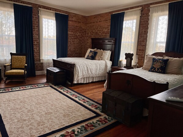 A bedroom with a brick wall, two beds, a wooden chair, a bench, and a floral rug.