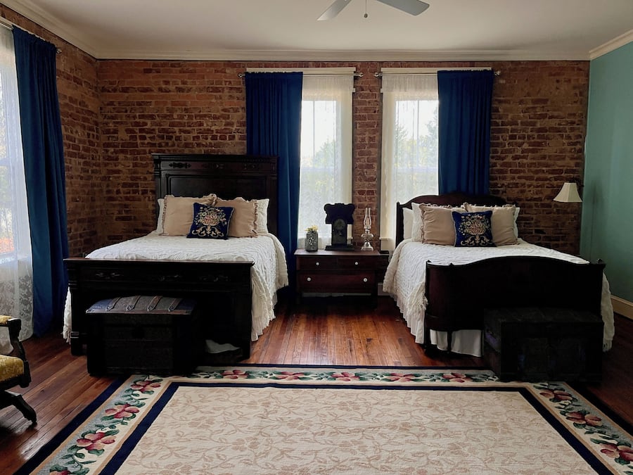 Quarto com duas camas, piso de madeira, parede de tijolos e tapete com padrão floral.