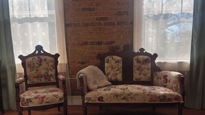 A room with a brick wall, two wooden chairs with floral upholstery, and a matching sofa. - Tanglewood Inn (Greenville)