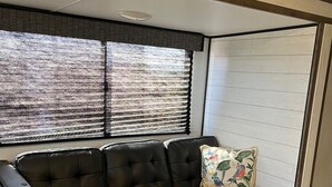 En sort lædersofa med et blomstret pude, en vævet måtte og et vindue med persienner.