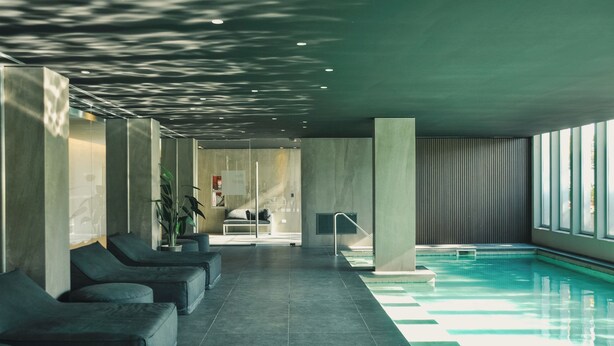 Ein moderner Poolbereich im Innenbereich mit Liegestühlen, einer Glastrennwand und Blick auf den Pool.