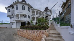 A multi-story white building with a stone retaining wall, a staircase, and a gated entrance. - Awaii Jamaica (Montego Bay)