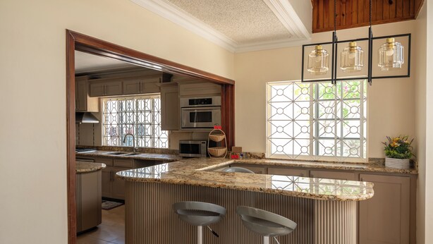 A modern kitchen with a central island, bar stools, stainless steel appliances, and a large window with decorative glass. - Awaii Jamaica (Montego Bay)