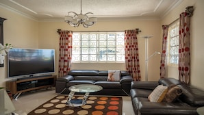 A living room with a leather sofa, a glass coffee table, a flat-screen TV, and a patterned rug. - Awaii Jamaica (Montego Bay)