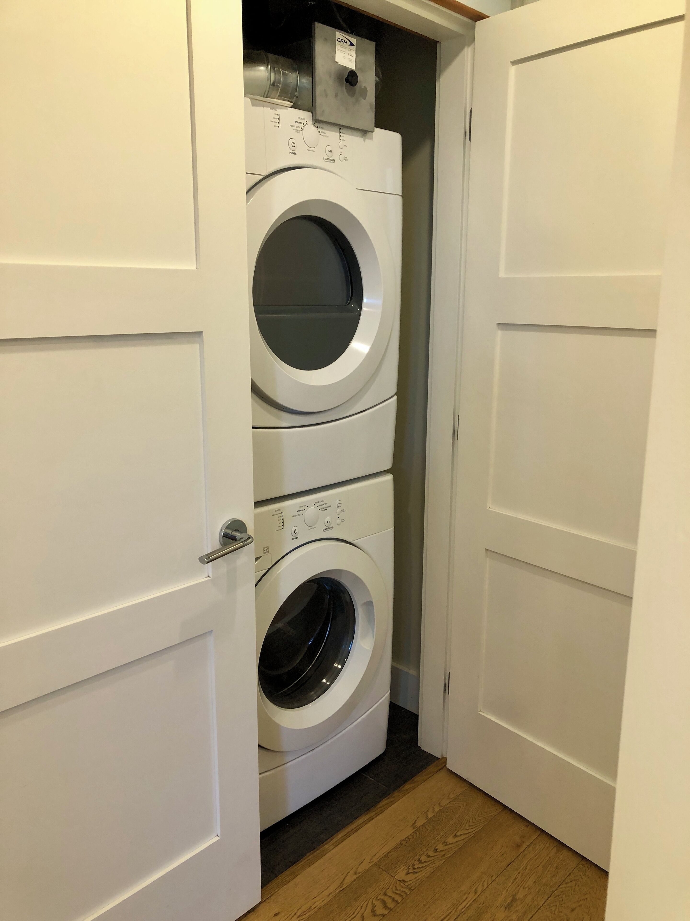 A laundry room with two stacked front-loading washing machines and a control panel above them.