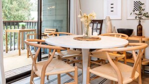 A dining area with a round table, wooden chairs, a white pendant light, and a view of the outdoors through a sliding glass door.