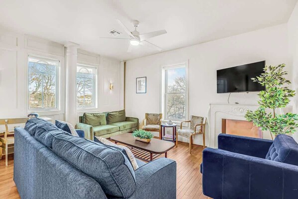 A living room with a sofa, chairs, a coffee table, a fireplace, and a TV. - Spacious 4BR Duplex · 5 Blks 2 Beach · Badges Incl (Asbury Park)
