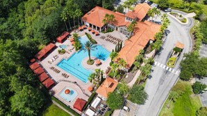 An aerial view of a resort with a swimming pool, lounge areas, and a parking lot.