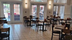 A spacious indoor dining area with multiple tables and chairs, large windows, and a ceiling fan.