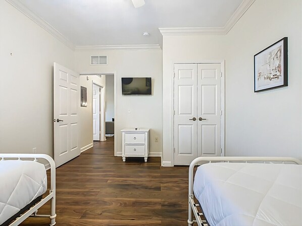 Un dormitorio con dos camas, una mesita de noche, un aparador y un televisor en la pared.