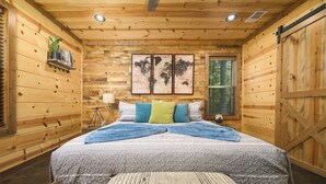 Une chambre à coucher dans une cabane en bois, avec un lit, des oreillers, un banc, une carte du monde accrochée au mur et une fenêtre.