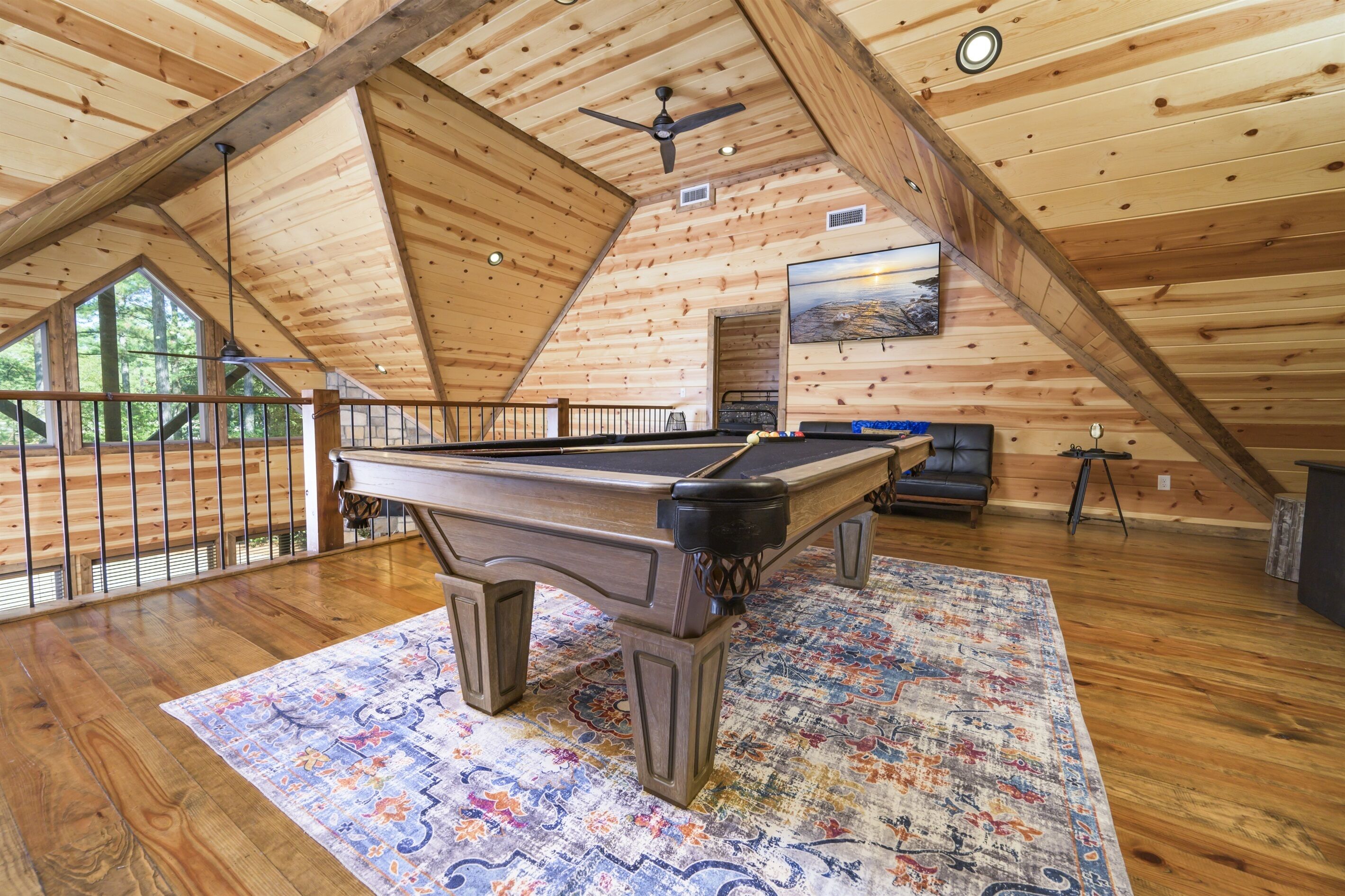 A wooden interior with a pool table, a ceiling fan, and a large window.
